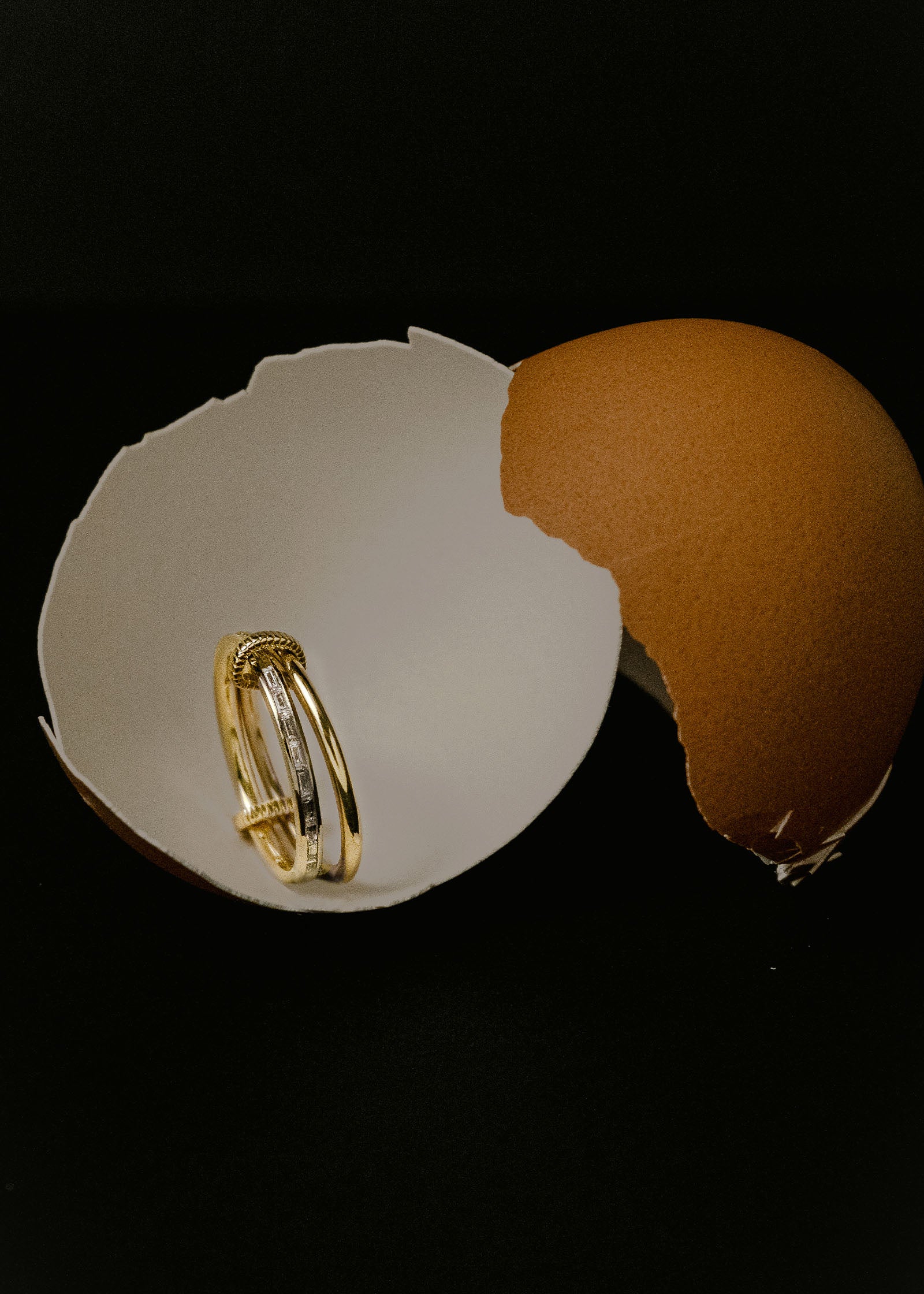 A Kinn 14k Gold Donna Linked Baguette Band Ring featuring 2 rings linked together sitting in an empty eggshell against a black background