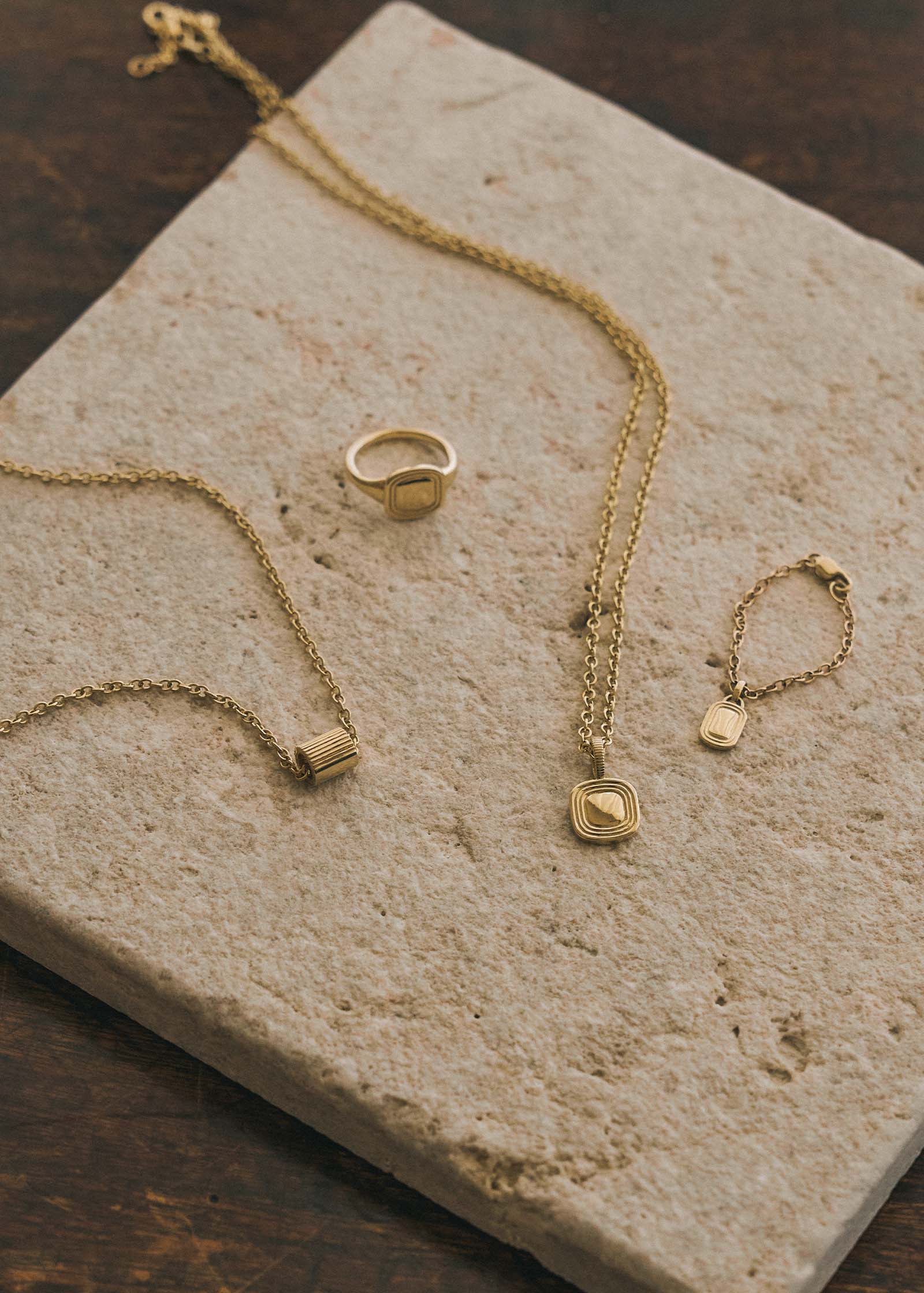 A Kinn x Shoppe Amber Interiors The Estate Pendant Necklace 14k Yellow Gold laying flat with The Estate Signet Ring, Estate Watch Charm, and Estate Charm on a Cable Rolo Chain on a stone slab
