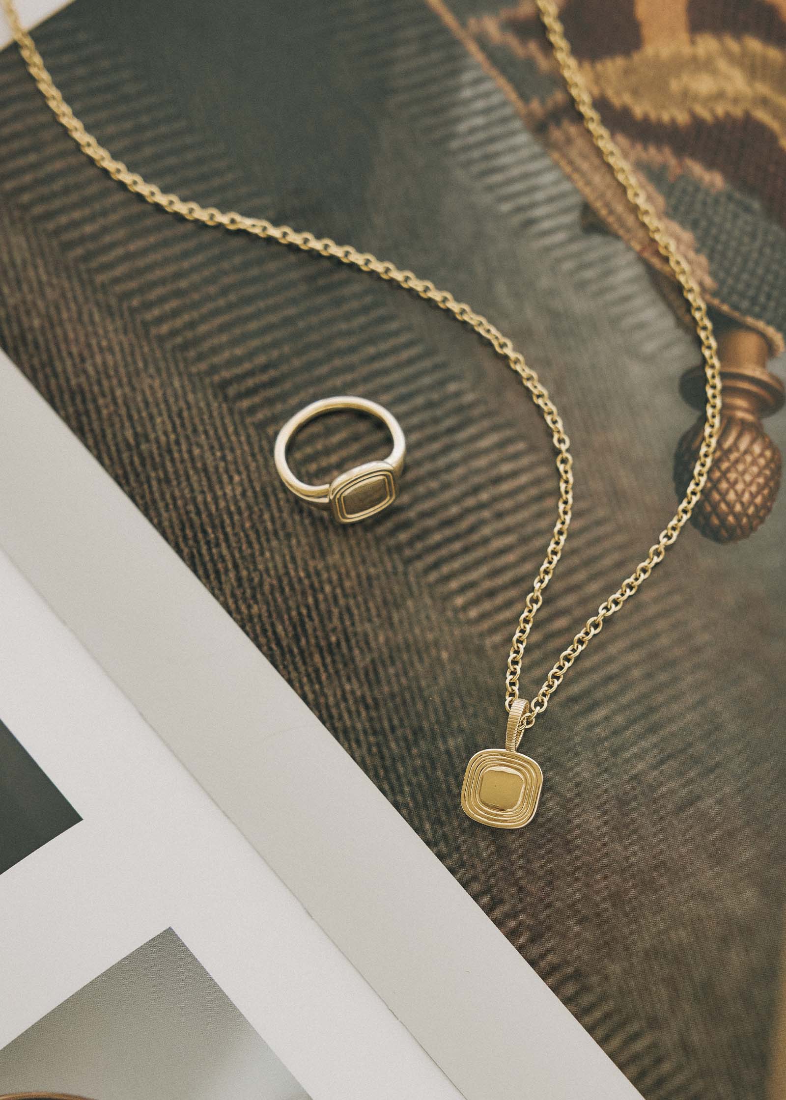 Kinn x Shoppe Amber Interiors The Estate Pendant Necklace 14k Yellow Gold laying flat with The Estate Signet Ring on an open book