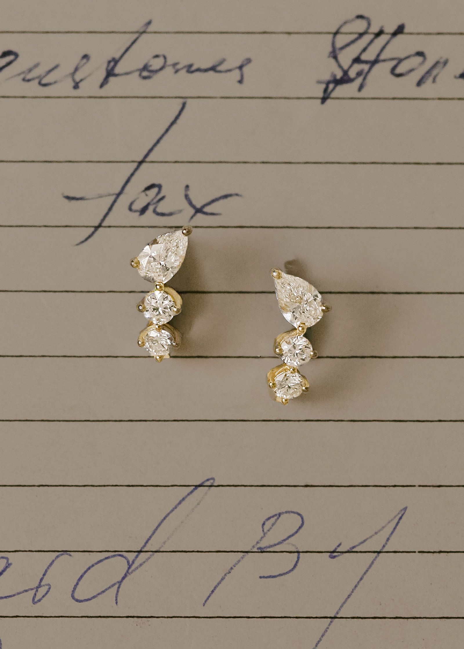 a pair of Kinn 14k Gold Jules Mixed Diamond J-Hoop Earrings laying against a lined sheet of paper with writing