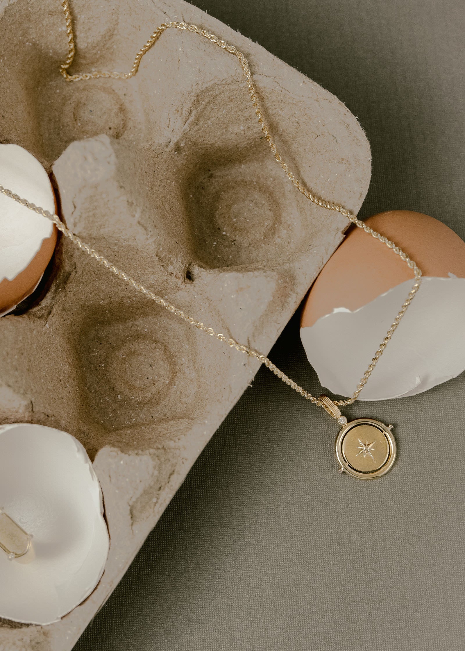 A Kinn 14k Gold Round North Star Birthstone Necklace Diamond on a Petite Rope Chain draped across an egg carton with broken egg shells