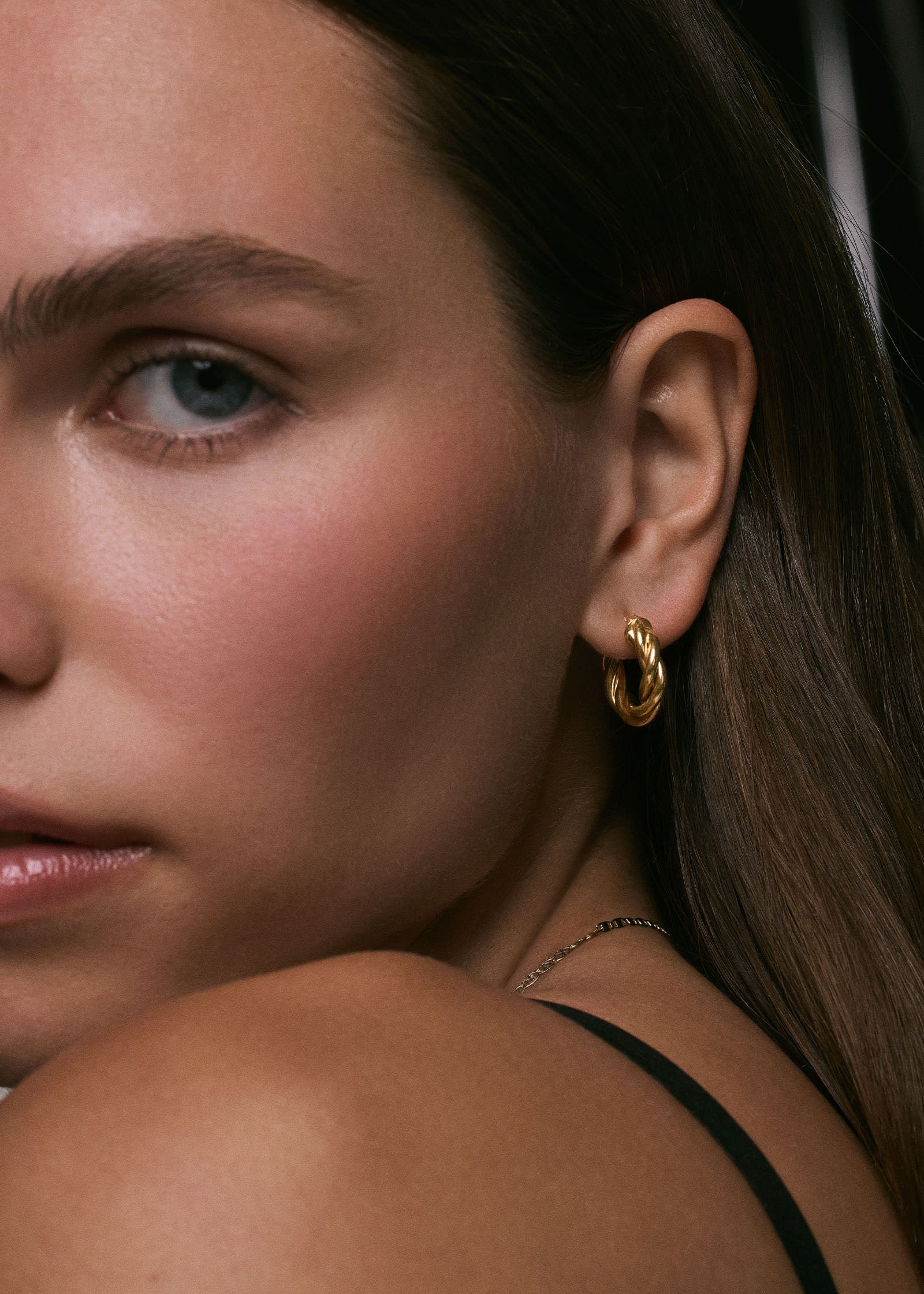 A close up of a woman wearing Kinn 14k Gold Taylor Twist Petite Hoop Earrings