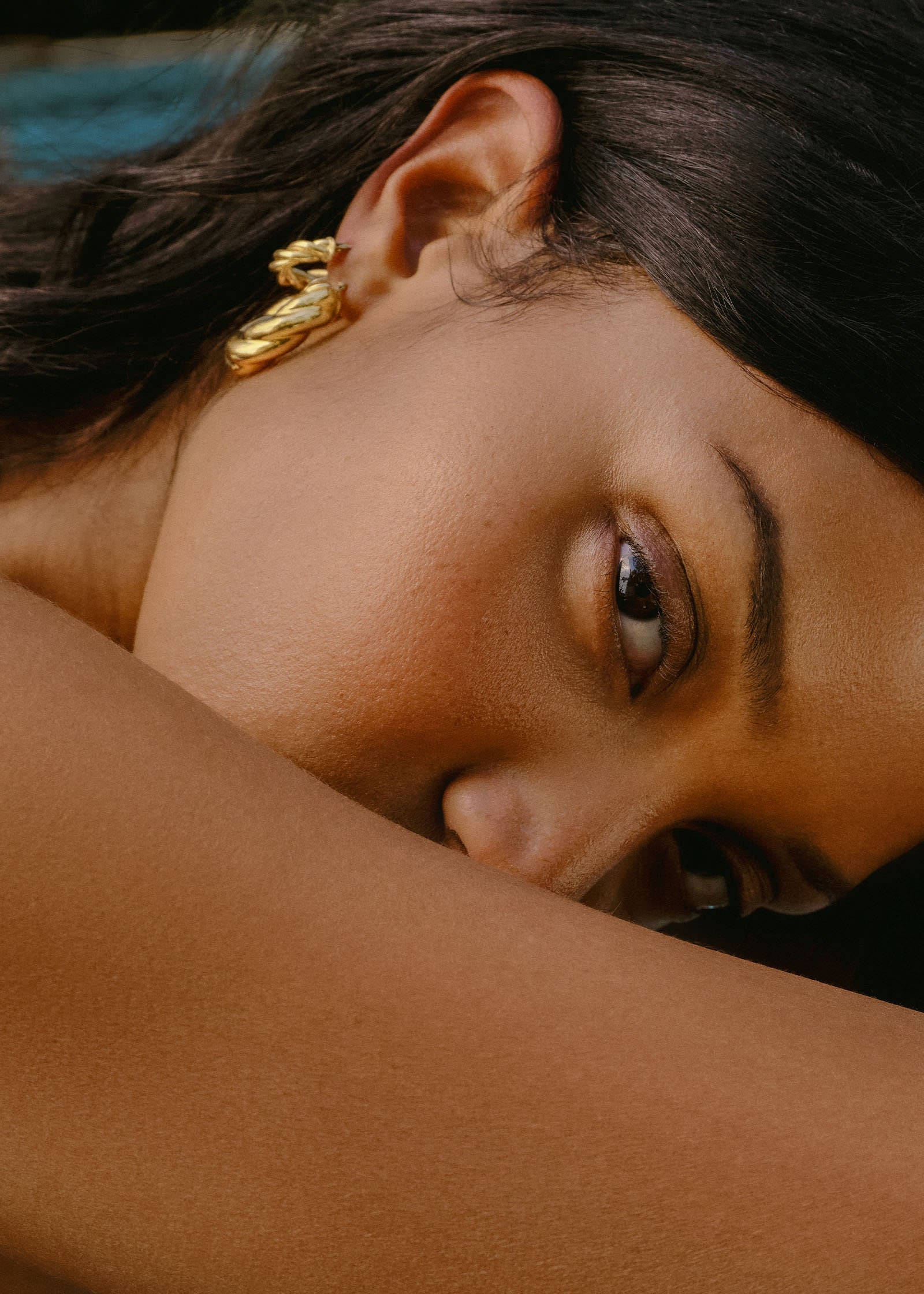 woman with her head resting downwards wearing a Kinn 14k Gold Taylor Twist Petite Hoop Earring in her second piercing layered with a Taylor Twist Hoop