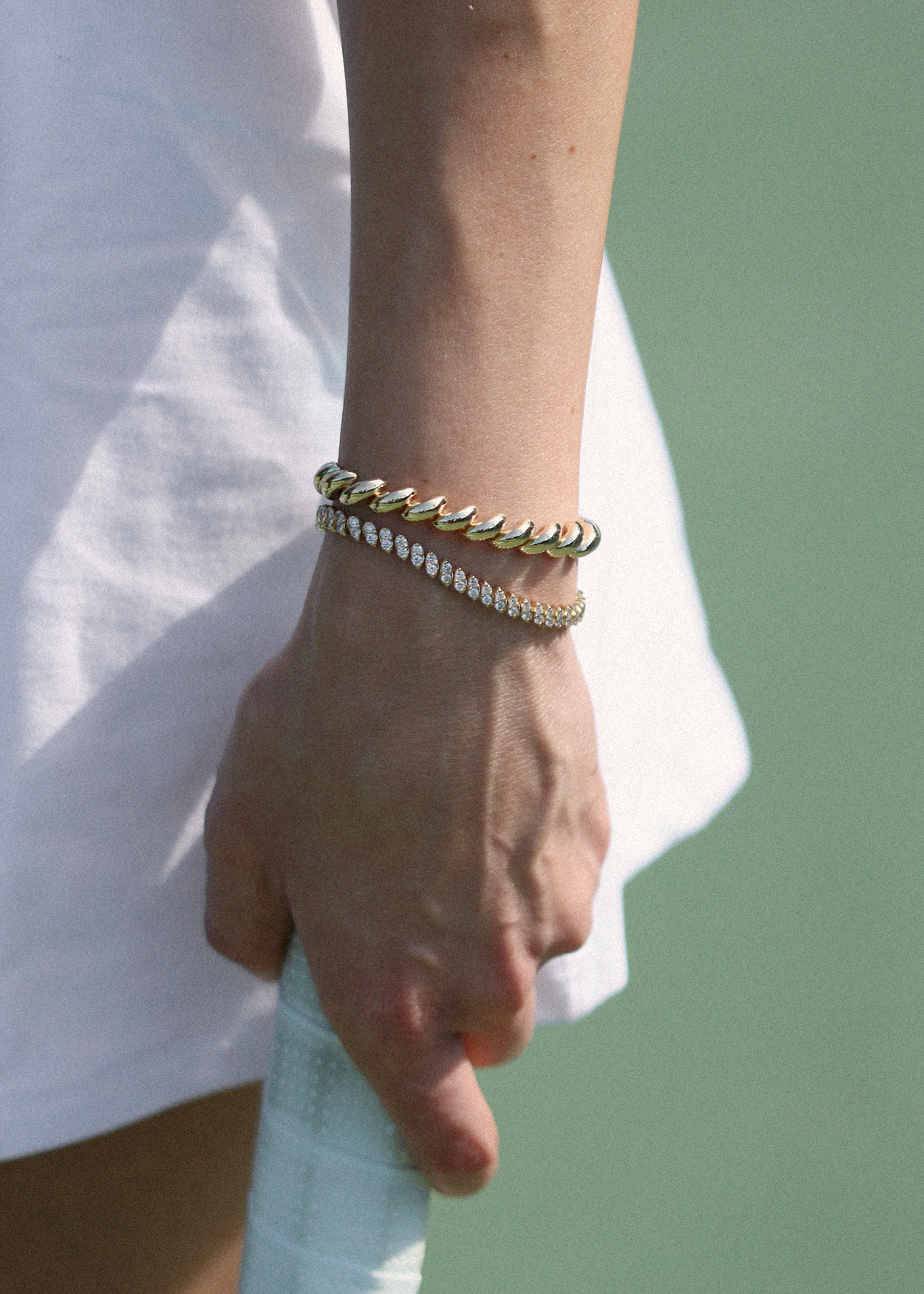 woman in tennis gear wearing a Kinn Studio 14k Gold Hampshire House Bracelet layered with a Sofia Marquise Diamond Tennis Bracelet holding a tennis racket