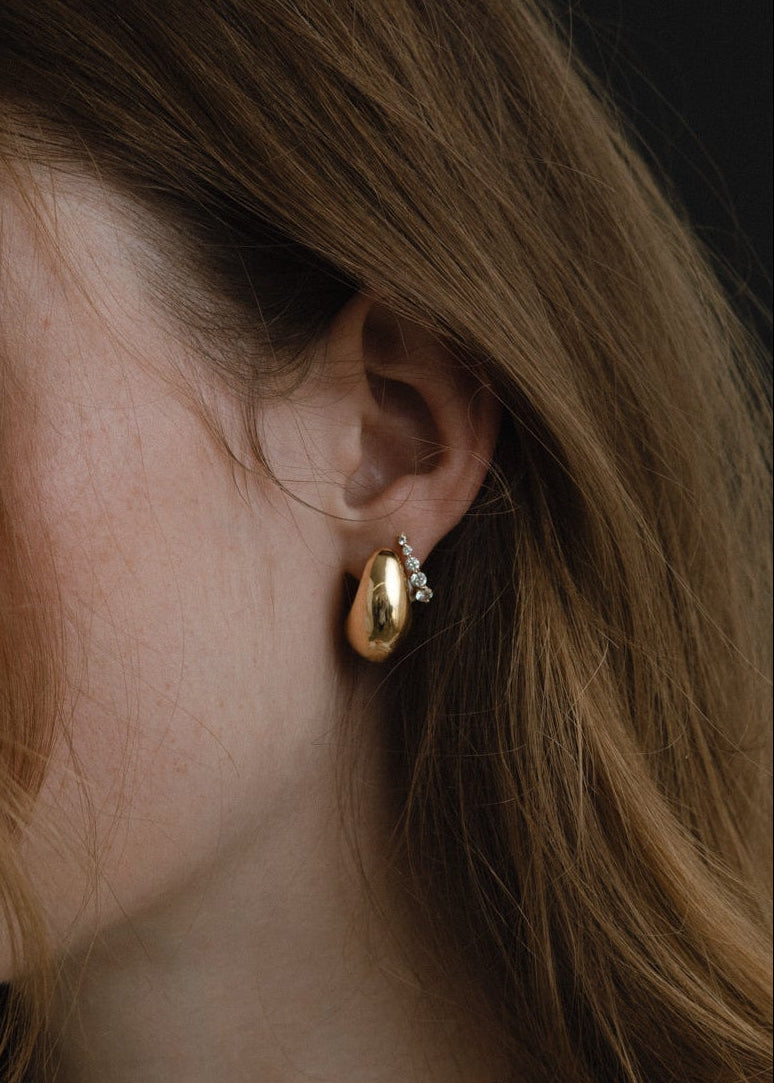 close up of a woman's ear wearing a Kinn 14k Gold Petite Bold Teardrop Hoop Earring with a Graduated Diamond Huggie Earring