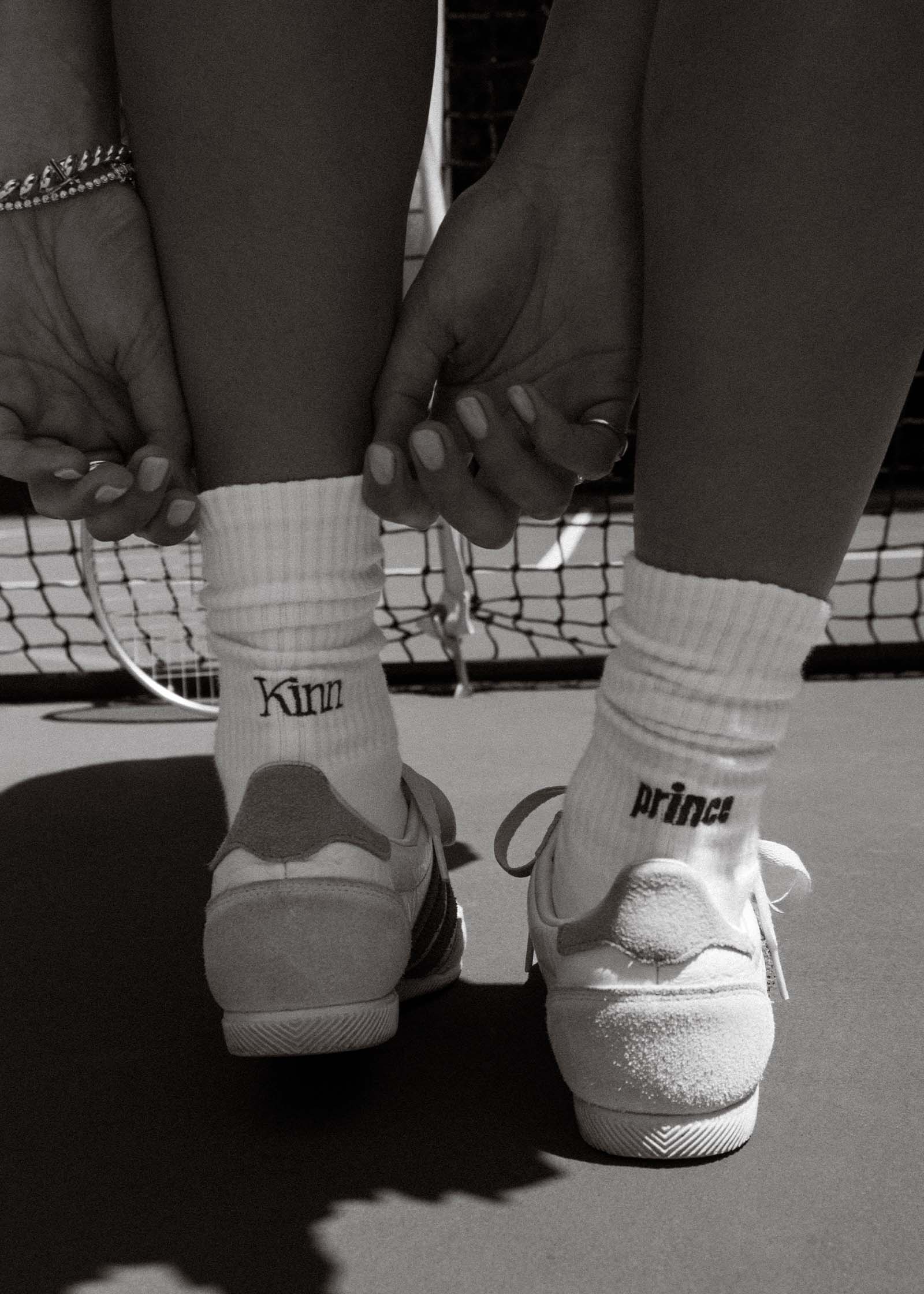 Black and white photo of a woman wearing Kinn x Prince Crew Socks on a tennis court