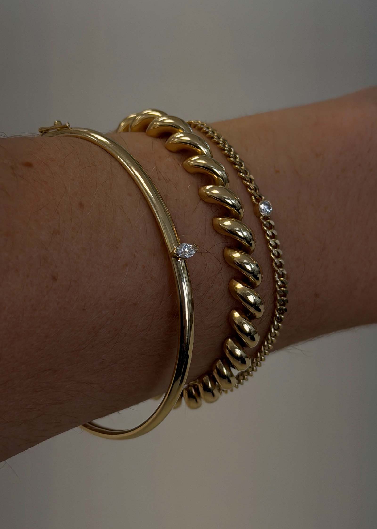 woman's wrist wearing a Kinn Vintage 14k Gold Bangle with Marquise Diamond stacked with a Hampshire House Bracelet
