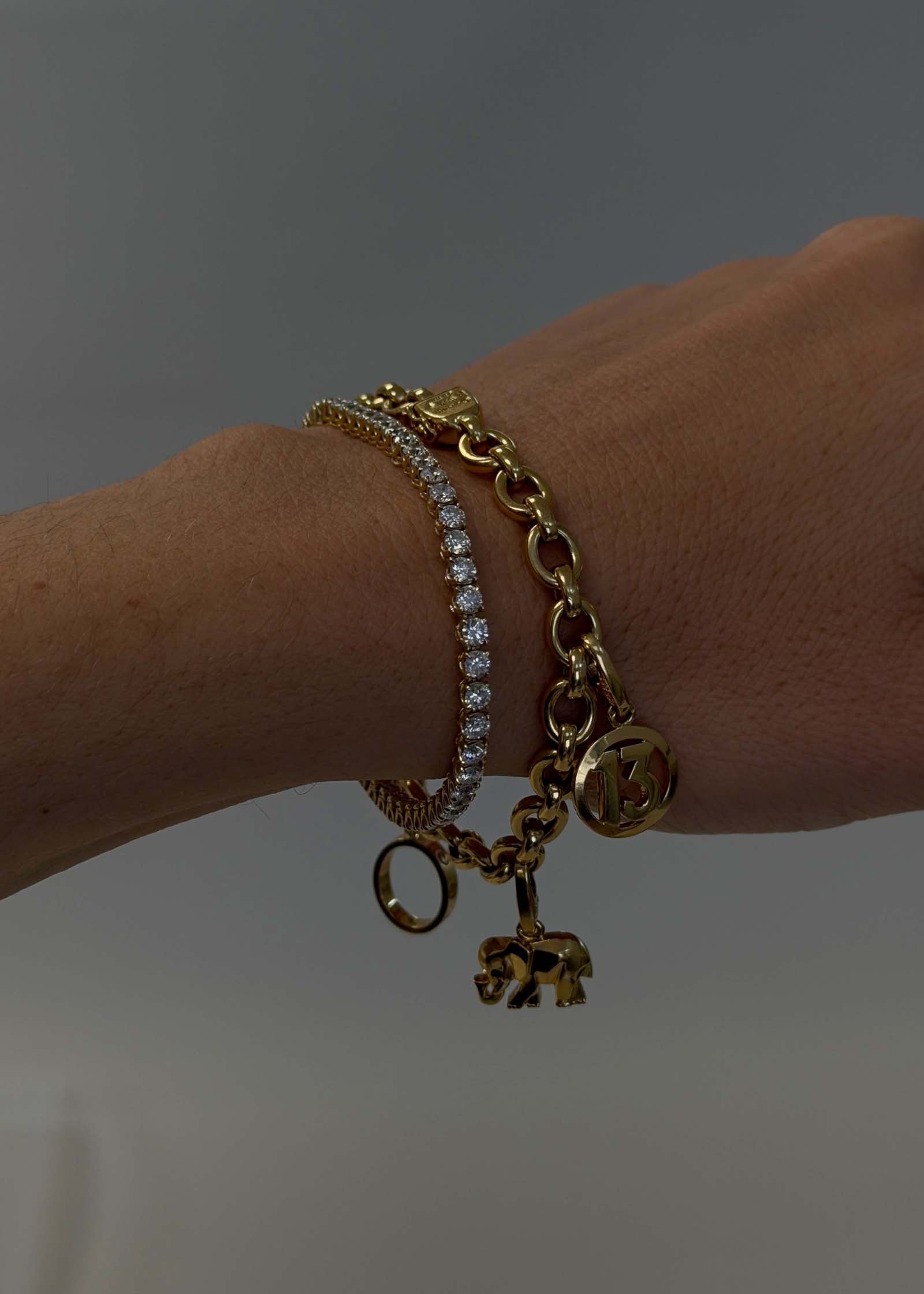 woman's wrist wearing a Kinn Vintage 18k Gold Cartier Charm Bracelet stacked with a diamond tennis bracelet