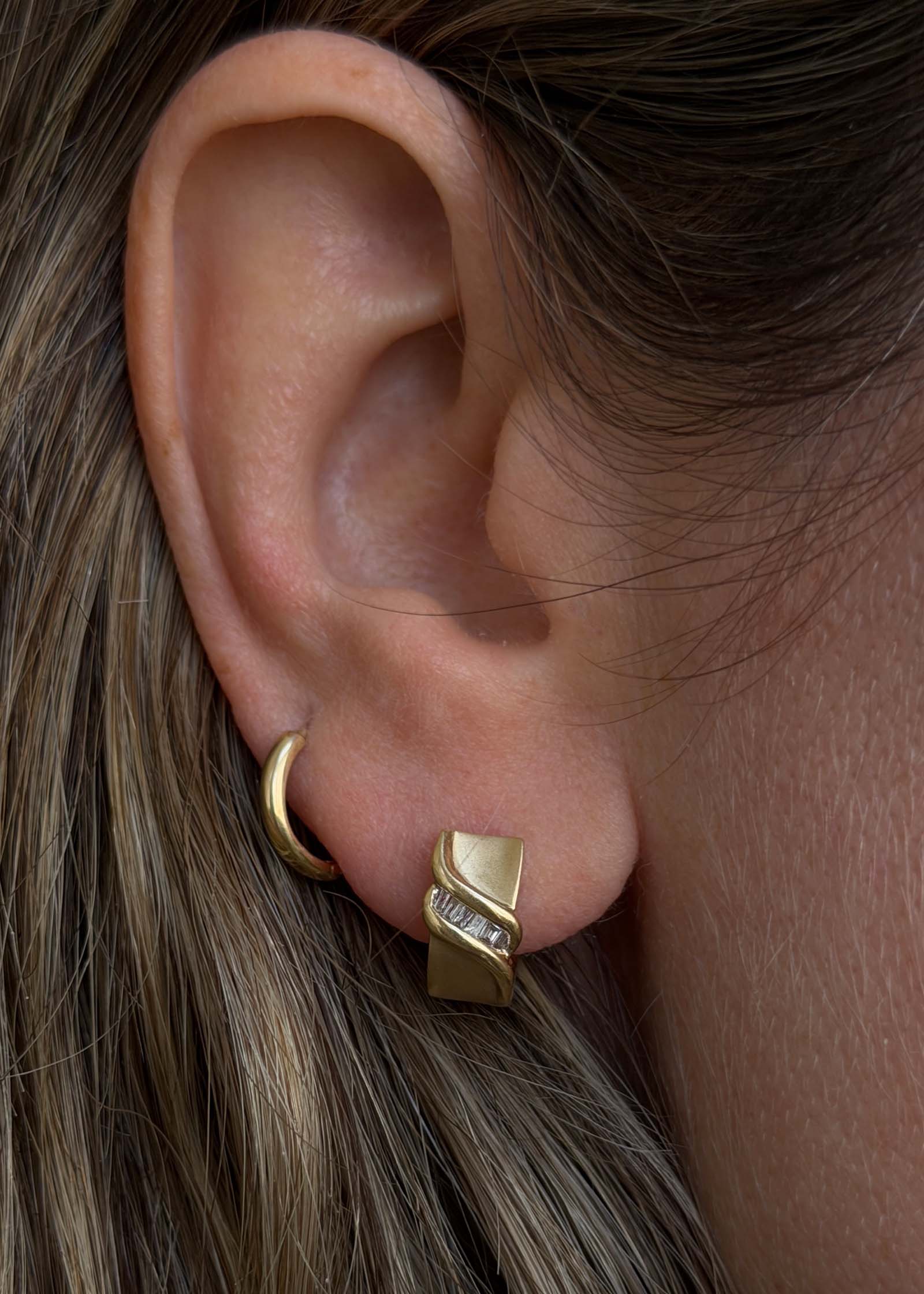close up of woman's ear wearing Kinn Vintage 14k Gold Baguette Diamond Huggie Earrings