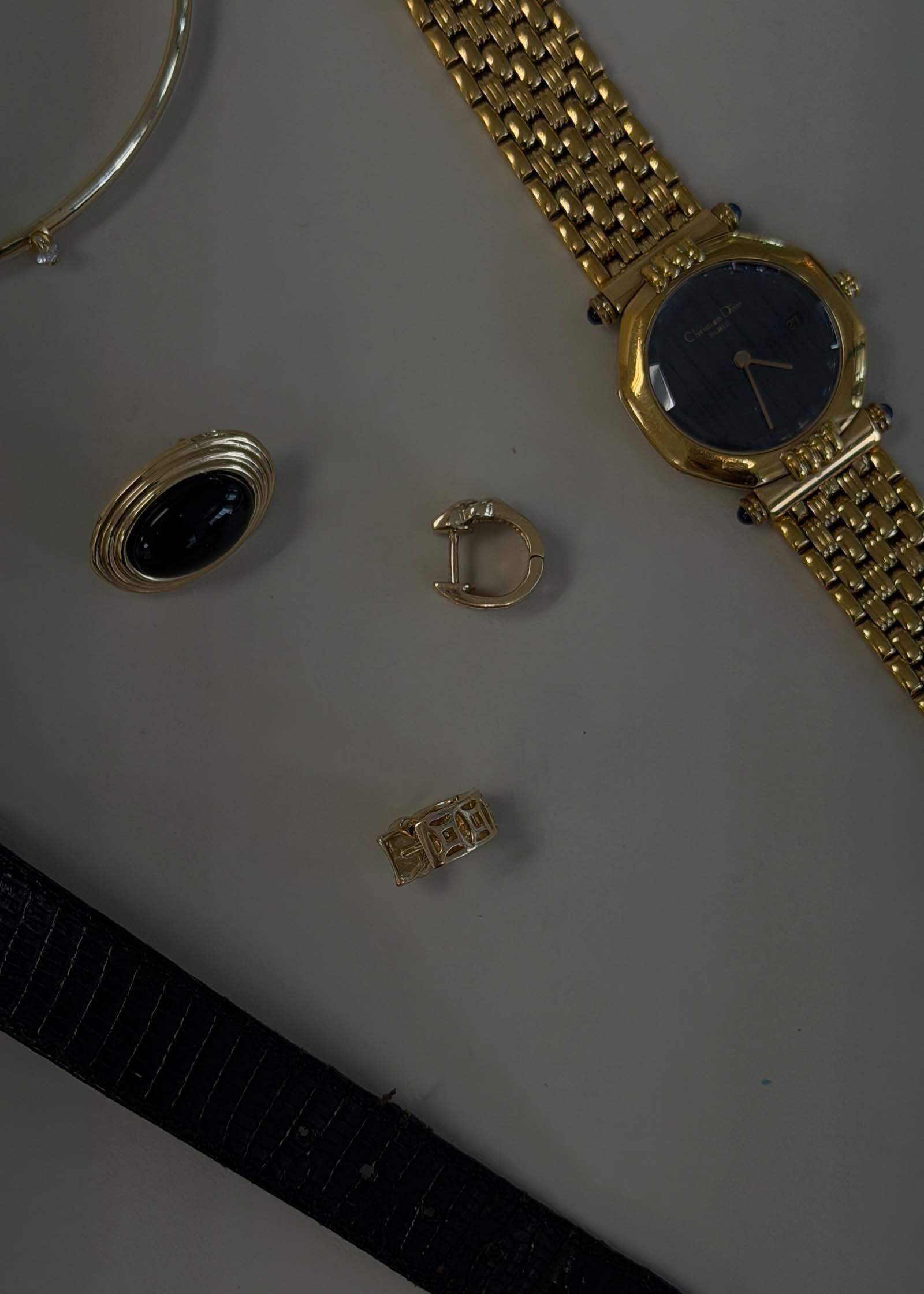 Flat lay of Kinn Vintage 14k Gold Baguette Diamond Huggie Earrings with a Dior watch and vintage onyx earring