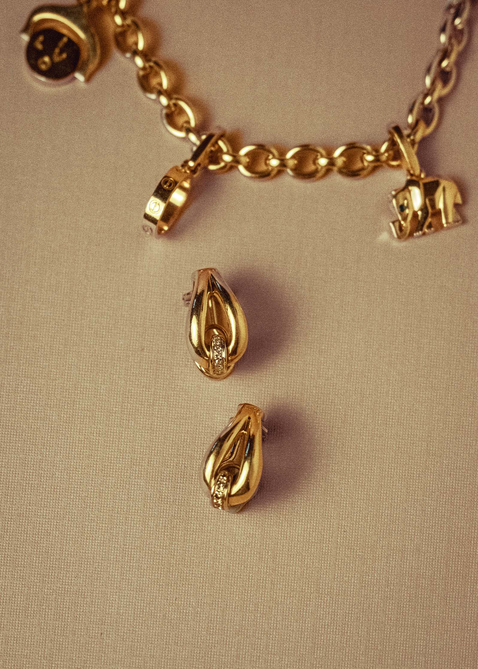 Kinn Vintage 18k Gold Tubular Teardrop Pavé Earrings laid flat next to a vintage Cartier charm bracelet